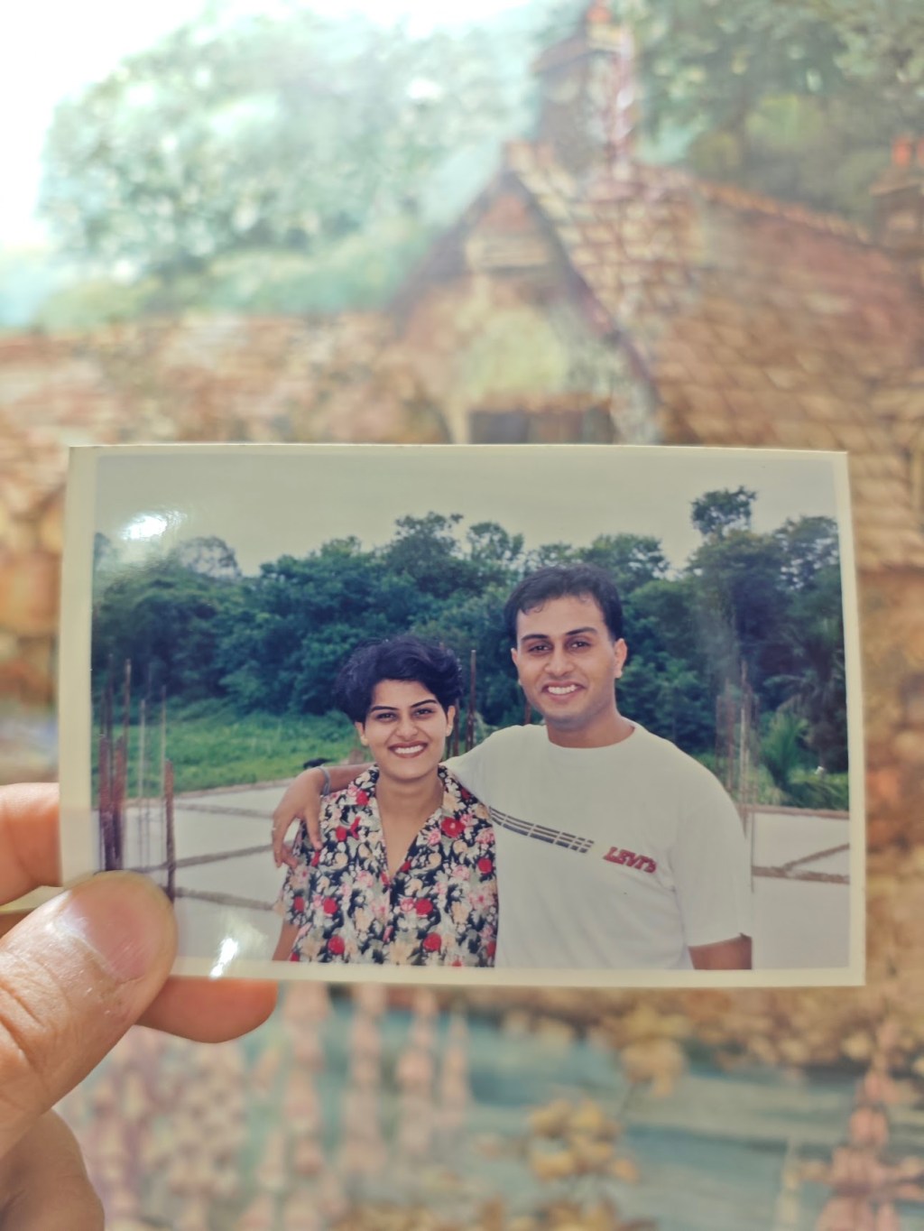 An old printed photograph of two siblings as young adults, held up against the same location years later