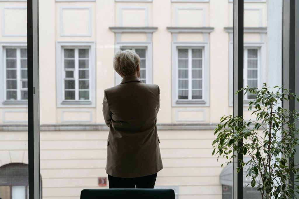 Woman in a blazer standing by a window, reflecting on leadership in the age of AI