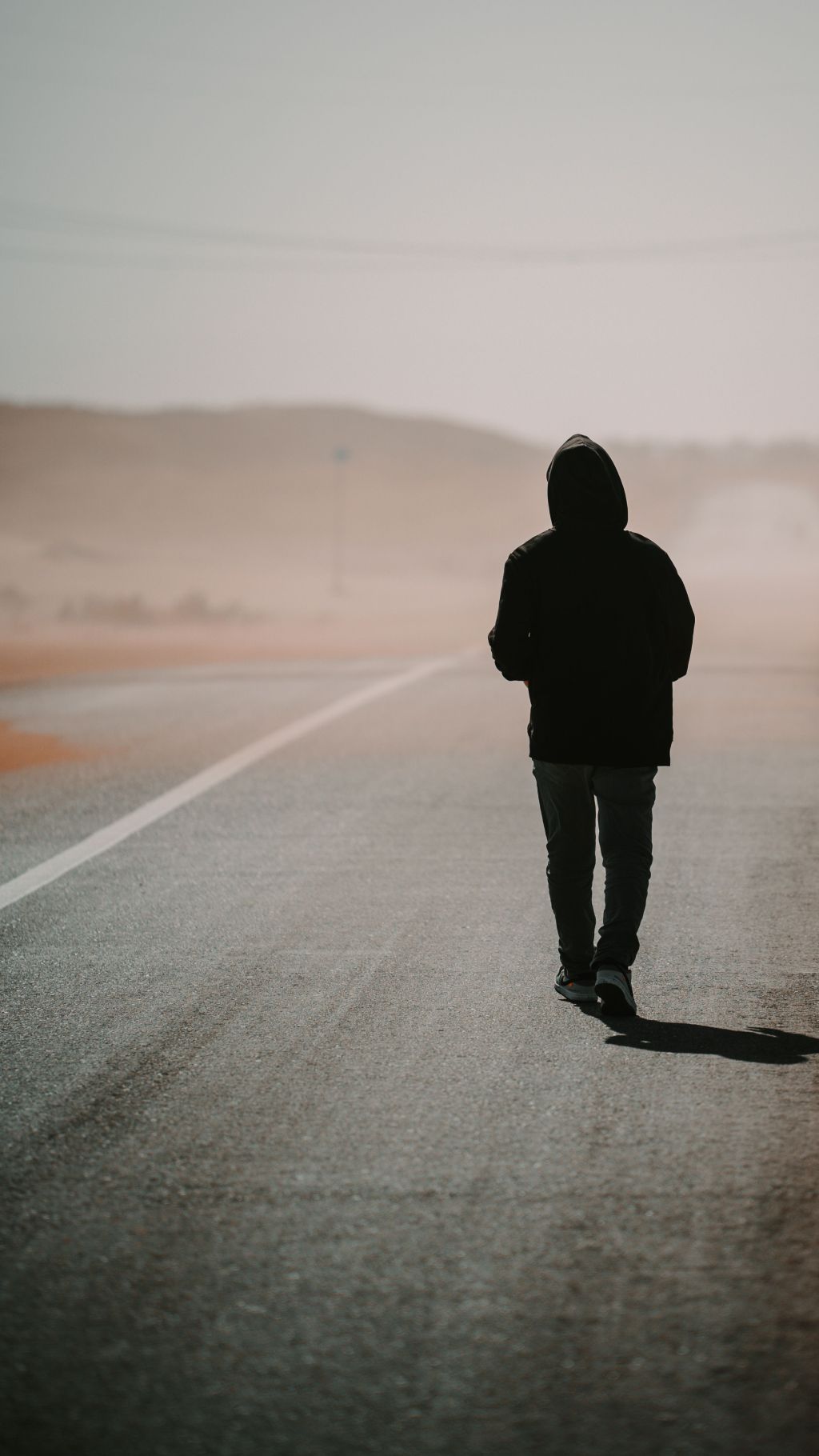 A solitary hooded figure walking alone down a foggy open road